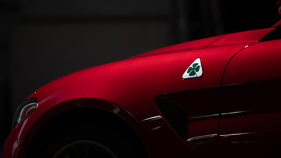 Side angle of a red Giulia Quadrifoglio against a dark background, with focus on the front tire and driver’s side door.